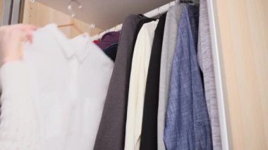 Gardıropta yer düzenleme kavramı. Koyu renk ve açık renkli giysiler dolapta düzgünce asılı. Kadının eli elbiseyi seçer..