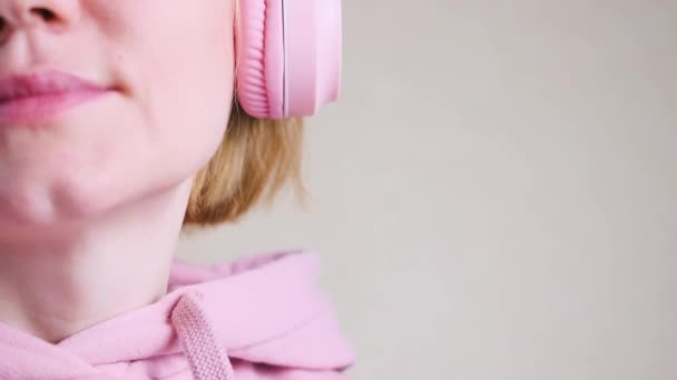 穿着粉色运动衫的白人女孩 背景和粉色耳机的色调相似 音乐的概念 有声读物 世界音乐日 世界摇滚日 — 图库视频影像