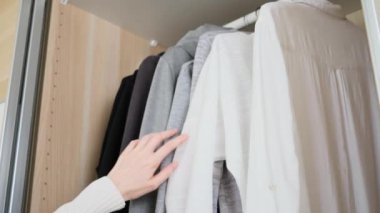 Gardıropta yer düzenleme kavramı. Koyu renk ve açık renkli giysiler dolapta düzgünce asılı. Kadının eli elbiseyi seçer..