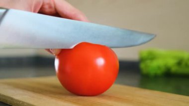 Bıçaklı eller taze olgun bir domatesi tahta bir kesme tahtasıyla kesti. Sağlıklı yemek, yemek pişirme, vejetaryenlik, taze sebze, mutfak.