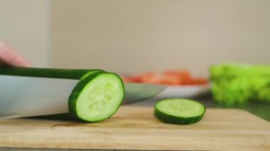 Bıçaklı eller taze olgun bir salatalığı tahta bir kesme tahtasıyla kesti. Sağlıklı yemek, yemek pişirme, vejetaryenlik, taze sebze, mutfak.