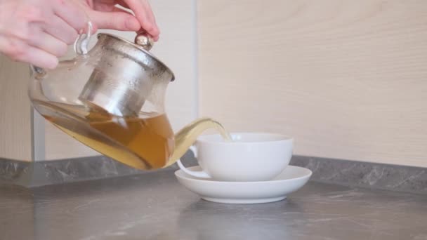 A női kezek főtt teát öntenek egy fehér csészébe és csészealjba. A teaivás, a gyógynövény egészséges tea fogalma