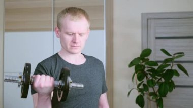 Kafkas asıllı sportmenliğe aykırı sarışın bir adam, dambılı kollarını eğitiyor. Evde spor konsepti, tecrit.