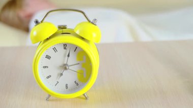 Sarı alarmlı saati kapat. Arka plandaki kadın uyanıyor ve alarmı kapatıyor. Sabah konsepti, uyanış..