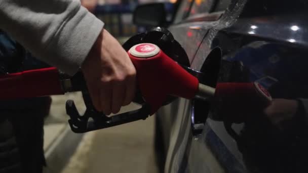 一个人手里拿着一支加满油的枪插在汽车的油箱里 晚上好燃料 汽车概念 — 图库视频影像