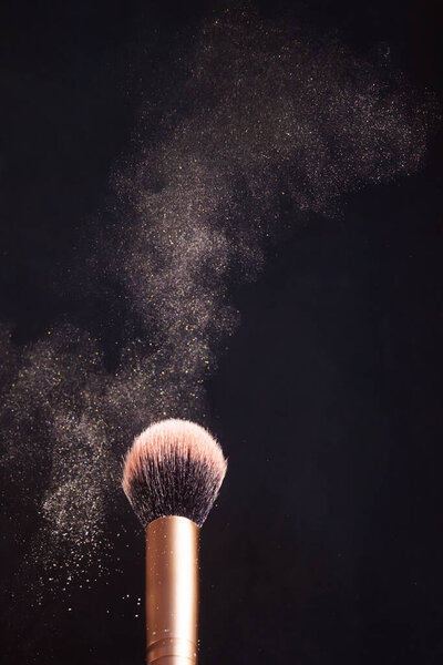 Makeup brush with a highlighter that effectively spreads in different directions. Dark background, minimalism, copy space. Make-up, cosmetics, visage concept.