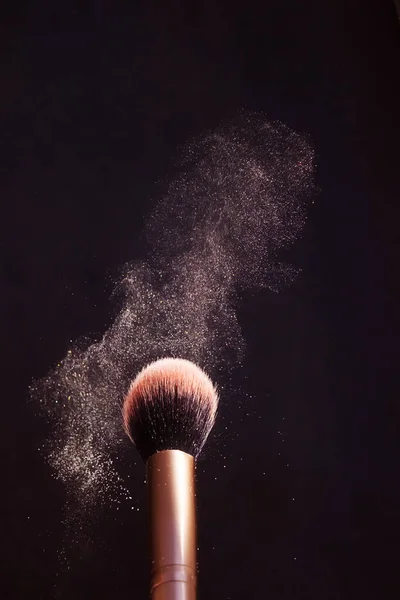 Makeup brush with a highlighter that effectively spreads in different directions. Dark background, minimalism, copy space. Make-up, cosmetics, visage concept.