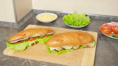 Eller, tahta kesme tahtasından taze yapılmış sebzeli, jambonlu ve peynirli sandviçleri topluyor. Evde basit yemekler pişirmek, atıştırmalıklar..
