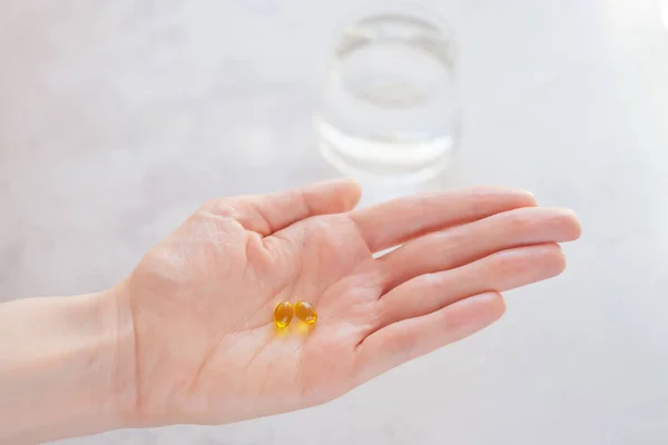 Açık arkaplanda sarı renkli vitaminler. Arkasında bir bardak su var. Vitamin alma konsepti, beslenme takviyeleri, sağlık tanıtımı.