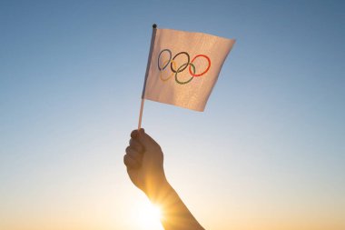 Küçük Olimpiyat bayrağı mavi gökyüzünün zeminine ve batan güneşe karşı dalgalanıyor. Kış ve Yaz Olimpiyat Oyunları Konsepti, 2021, 2022.