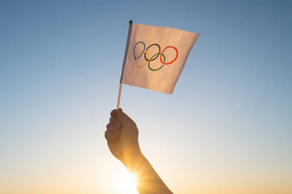 Küçük Olimpiyat bayrağı mavi gökyüzünün zeminine ve batan güneşe karşı dalgalanıyor. Kış ve Yaz Olimpiyat Oyunları Konsepti, 2021, 2022.