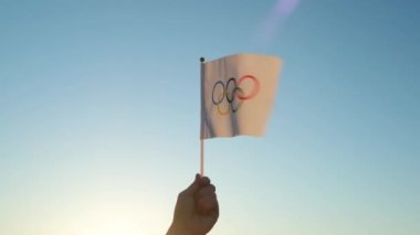 Küçük Olimpiyat bayrağı mavi gökyüzünün zeminine ve batan güneşe karşı dalgalanıyor. Kış ve Yaz Olimpiyat Oyunları Konsepti, 2021, 2022.