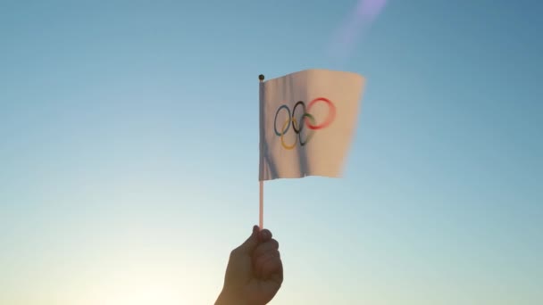 Ολυμπιακή Σημαία Μικρή Στο Χέρι Κυματίζει Στο Φόντο Του Γαλάζιου — Αρχείο Βίντεο