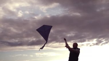 Mavi uçurtma günbatımında gökyüzünde süzülüyor. Adam uçurtmayı yönetiyor. Özgürlük kavramı, yaz hobileri, doğada eğlence. Minimalizm, metin için alan, mavinin tonları. Siluet