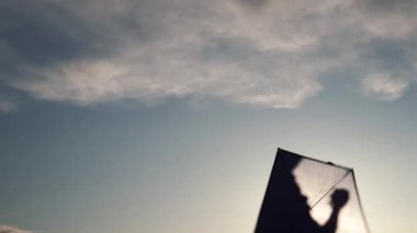 Mavi uçurtma günbatımında gökyüzünde süzülüyor. Adam uçurtmayı yönetiyor. Özgürlük kavramı, yaz hobileri, doğada eğlence. Minimalizm, metin için alan, mavinin tonları. Siluet