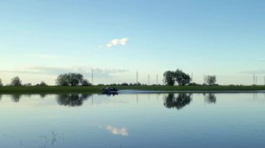 Küçük bir balıkçı teknesi dar bir nehir boyunca tarlalara ve ağaçlara karşı yüzüyor. Su taşımacılığı kavramı, doğa. - Khanty-Mansiysk, 10 Haziran 2021