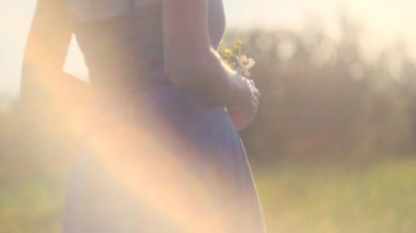 Woman's hands with a small bouquet of wild flowers close-up. Bright sunset sun in the field. Harmonious summer concept
