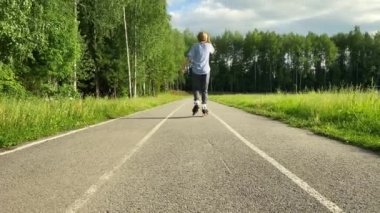 Siluetteki kadın silueti. Ormanda asfalt yol, güneş batıyor. Açık hava sporları ve eğlence konsepti.