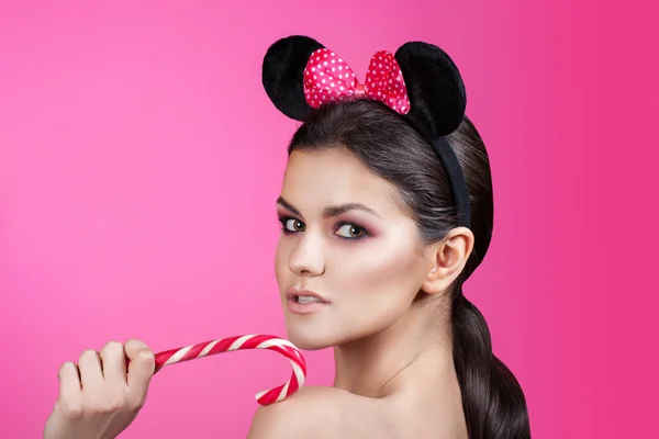 style woman portrait perfect face, professional make. fashion mouse with big ears. Fashion art photo in bright pink background. Girl holding licorice candy.