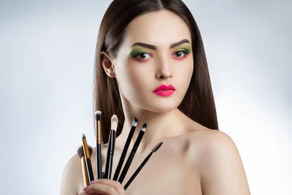 Young beautiful girl with bright makeup. A woman holds a professional makeup brushes — Stock Photo, Image