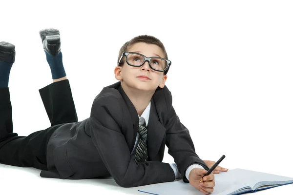 Cute smart boy in suit and tie lying on the floor. Boy writes in a notebook with a pencil — Stock Photo, Image