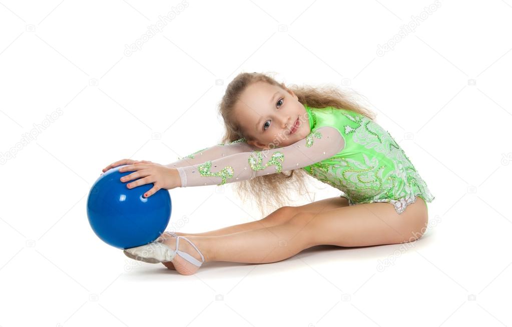 Gymnast cute little girl sitting on the floor. The child in the gymnastic suit with a blue ball in his hands