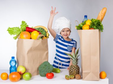 Onun el ve V Yaşasın gösteren ürünlerin büyük çanta ile Şef şapkalı küçük mutlu kız düzenlenen
