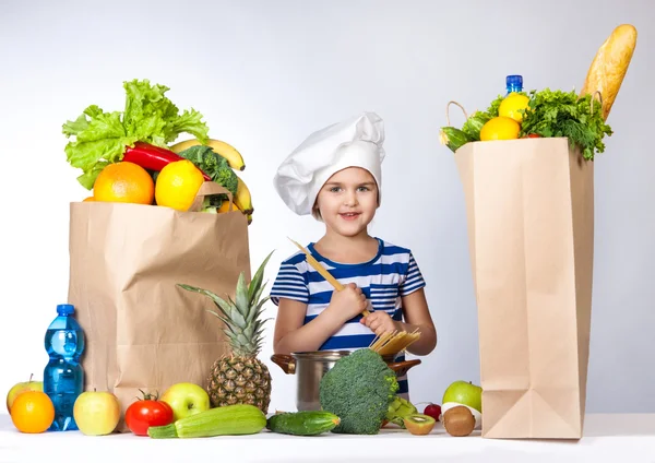 Little happy girl in chef hat with big bags of products. It keeps in the hands of spaghetti — Stock Image Little happy girl in chef hat with big bags of products. It keeps in the hands of spaghetti Stock Image