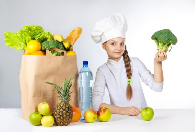 Bir kap içinde küçük mutlu kız taze gıda çeşitli yemek. Kız holding brokoli. ve gösterileri Tamam. Olumlu insan duygu, yüz ifadesi duygu, tutum. Taze sebze ve meyveler ile çanta.