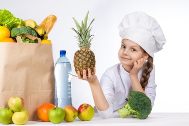 Bir kap içinde küçük mutlu kız taze gıda çeşitli yemek. Kız holding ananas. ve gösterileri Tamam. Olumlu insan duygu, yüz ifadesi duygu, tutum. Taze sebze ve meyveler ile çanta.