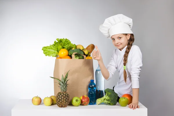 Little girl in a cap cook a variety of fresh food. Girl with a variety of fresh vegetables and fruits. Health, nutrition — Stock Photo, Image