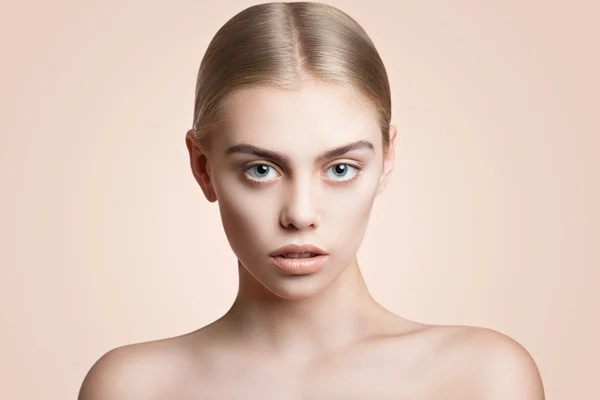 Retrato de una joven hermosa niña de cerca sobre un fondo beige. Cabello lamió hacia atrás, abrir los hombros, hermosos ojos azules, cosméticos y maquillaje —  Fotos de Stock