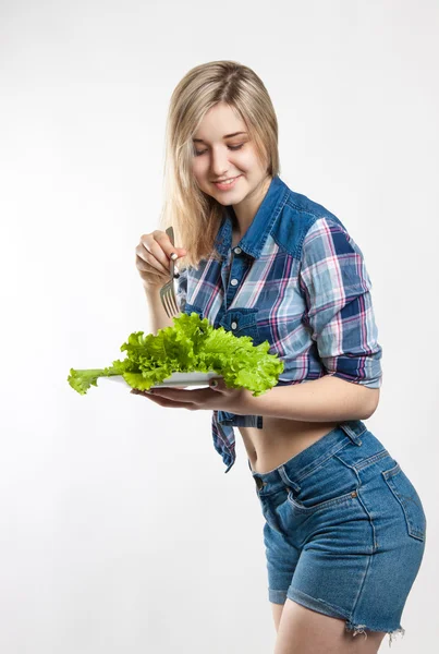 Молода щаслива жінка тримає свіжий зелений салат. Дівчина одягнена в сорочку і джинсові шорти. Харчування, дієта, втрата ваги — стокове фото