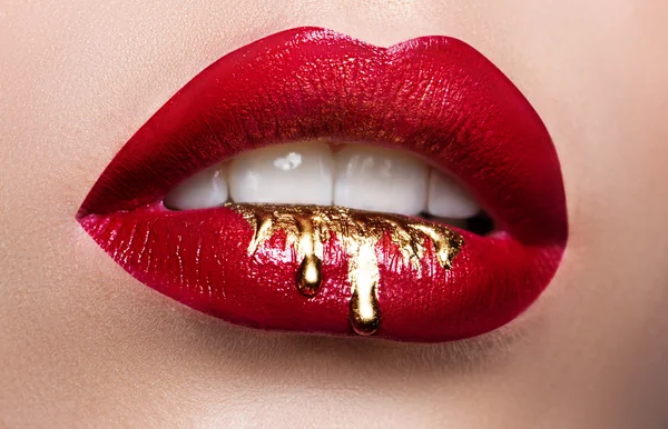 Prachtige vrouwelijke lippen close-up. Rode lippenstift, gouden verf stromen over zijn lippen. Stockfoto cosmetische reclame — Stockfoto