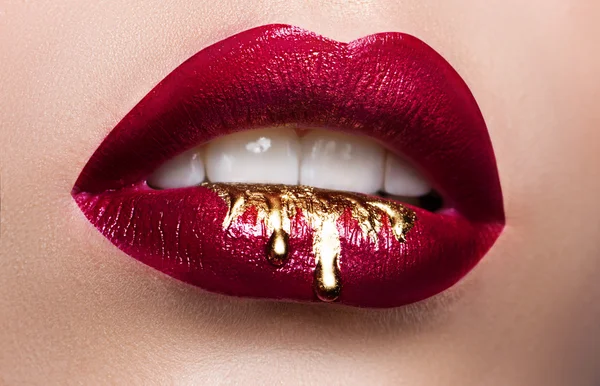 Hermosos labios femeninos de cerca. Lápiz labial rojo, pintura dorada que fluye sobre sus labios. Stock de Foto publicidad cosmética —  Fotos de Stock
