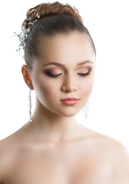 Porträtt av en ung flicka med en bröllop makeup. Perfekt hud, mjuka hår, stor kristall örhängen och hår prydnad. Isolering på vit bakgrund. Stockbild
