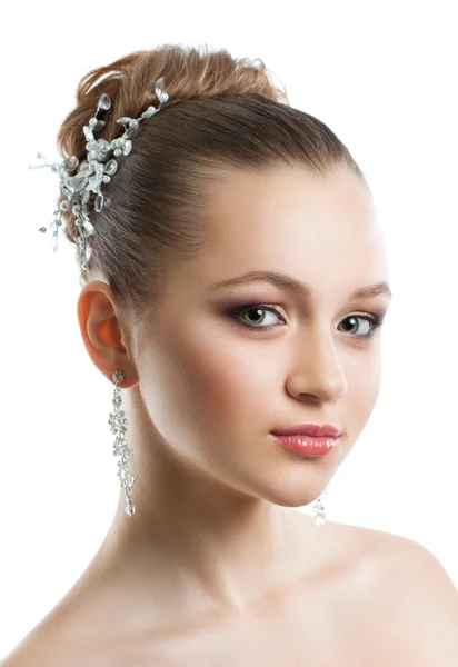 Porträtt av en ung flicka med en bröllop makeup. Perfekt hud, mjuka hår, stor kristall örhängen och hår prydnad. Isolering på vit bakgrund. Stockbild
