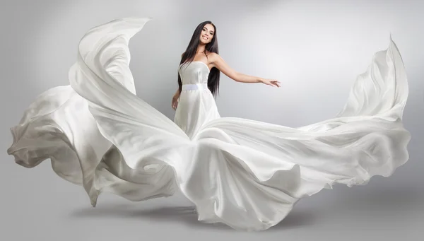 Mooi jong meisje in een witte jurk vliegen. Vloeiende weefsel. Lichte witte doek vliegen in de wind — Stockfoto