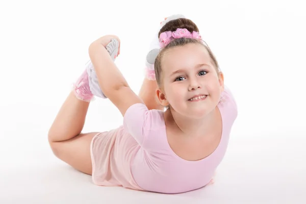 Küçük mutlu kız jimnastikçi bir egzersiz bacağını tutarak yere gerçekleştirir. Kız gülümsüyor. Esnek çocuk kostüm Spor eğitimi. — Stok fotoğraf