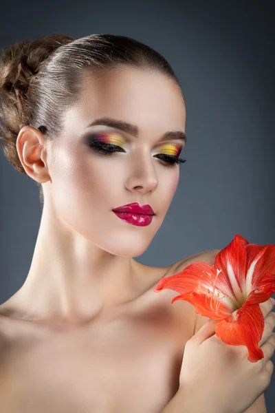Vacker kvinna med ljusa smink och röd blomma — Stockfoto