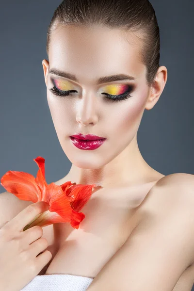 Όμορφη γυναίκα με φωτεινό μακιγιάζ και κόκκινο λουλούδι — Φωτογραφία Αρχείου