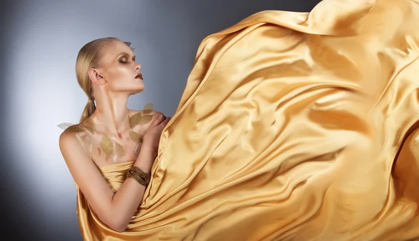 Beautiful woman in a flowing golden fabric — Stock Photo, Image