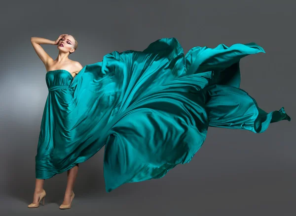 Frau im Seidenkleid, die im Wind weht. fliegendes und flatterndes Kleidtuch über grauem Hintergrund — Stockfoto