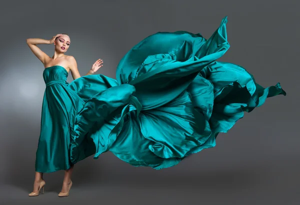 Frau im Seidenkleid, die im Wind weht. fliegendes und flatterndes Kleidtuch über grauem Hintergrund — Stockfoto