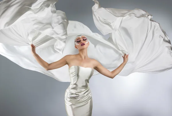 Mulher com maquiagem criativa brilhante em um pano branco voando. Uma menina segurando um pano branco voador — Fotografia de Stock