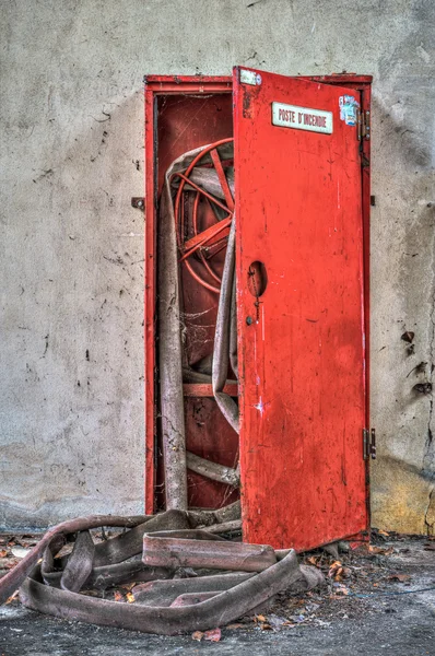 Разрушенный шкаф из красных пожарных шлангов на заброшенном заводе — стоковое фото