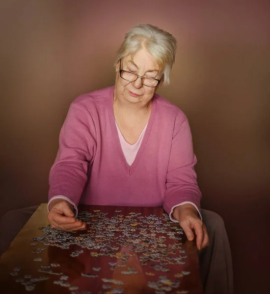 Grandmother is alone in the house playing jigsaw puzzles on the table.