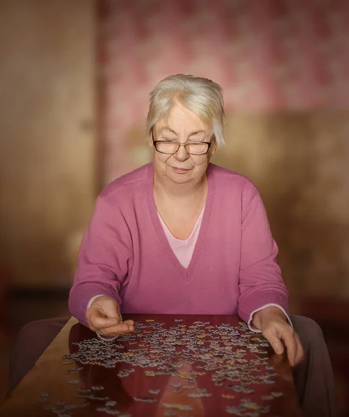 Grandmother is alone in the house playing jigsaw puzzles on the table.