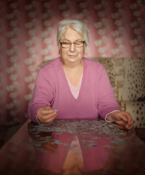 Grandmother is alone in the house playing jigsaw puzzles on the table.