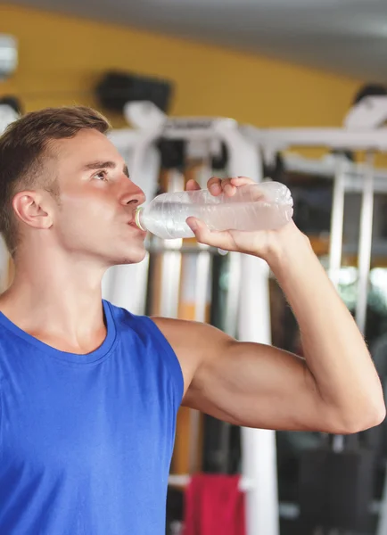 Hombre beber agua mineral en el gimnasio — Foto de Stock